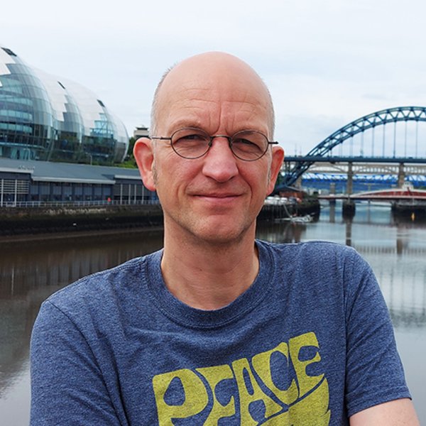 Foto von Thorsten Bonacker vor einer Brücke. Sein T-Shirt trägt die Aufschrift "PEACE".