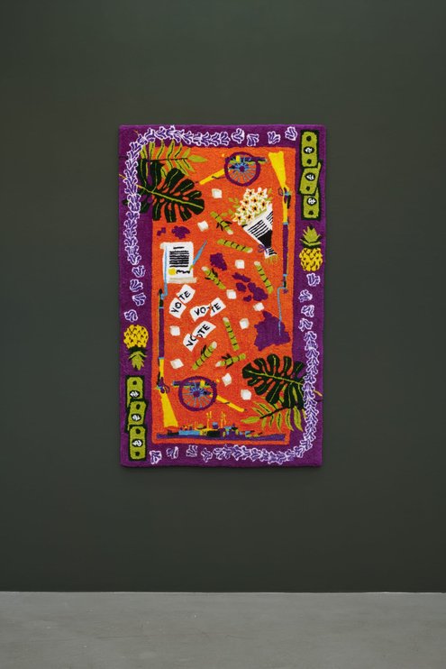 A very colorful carpet hangs upright on a black wall.