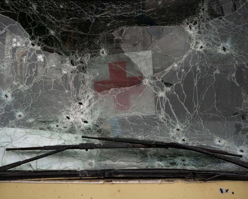 A pane of glass with bullet holes. Behind it, a red cross.